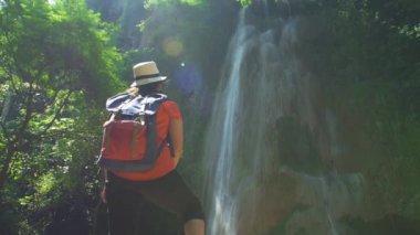 Sırt çantalı Asyalı kadının arkası. Kollarını aç, rahatla, şelaleye bakmaktan zevk al. Orman gezisinde yürüyüş yapan yürüyüşçüler Asya Tayland