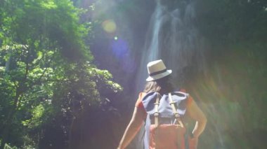 Sırt çantalı Asyalı kadının arkası. Kollarını aç, rahatla, şelaleye bakmaktan zevk al. Orman gezisinde yürüyüş yapan yürüyüşçüler Asya Tayland