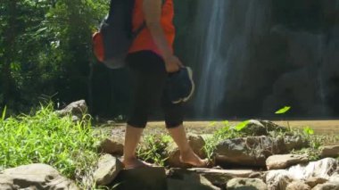 Sırt çantalı Asyalı kadın dereyi yalınayak geçmiş. Orman gezisinde yürüyüş yapan yürüyüşçüler Asya Tayland