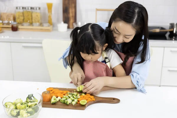 Happy Asian family Mother and child daughter are preparing the salad and cutting vegetables. cooking food in kitchen at home. Healthy food concept