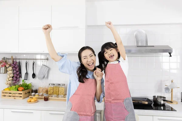 Portrait of Happy Asian family in the kitchen. Mother and Little girl in apron set good mood. Hands up Smile and glad