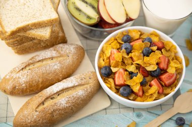 Sağlıklı kahvaltı. ekmek, meyve, çilek, yabanmersini, kivi, bardakta süt ve hasırda mısır gevreği ve ahşap masa. Arka plan Sağlıklı yiyecekler.