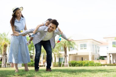 Mutlu Asyalı aile. Babası, kızına, güneş ışığının arka planında ve evinde bir parkta sırt sırta vermiş. Kopya alanı olan aile tatili kavramı