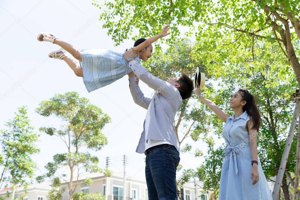Happy Asian family. Father throws up daughter in the sky in a park at natural sunlight background and house. Family vacation concept with copy space