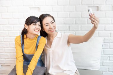 Mutlu Asyalı aile, anne ve genç kız. Evinde güneş ışığı olan bir odada kendinizin, selfie 'nizin ya da akıllı telefonunuzla fotoğraf çekin..