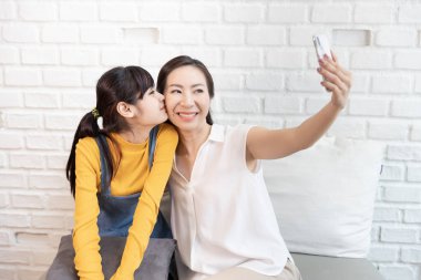 Mutlu Asyalı aile, anne ve genç kız. Evinde güneş ışığı olan bir odada kendinizin, selfie 'nizin ya da akıllı telefonunuzla fotoğraf çekin..