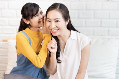 Asyalı bir aile, anne ve genç bir kız evde güneş ışığıyla bir odada dedikodu ve paylaşım yapıyorlar..