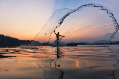 Alacakaranlıkta göldeki ahşap tekneye balık ağı atan Asyalı balıkçılar. Kavramsal Balıkçının kırsal yaşam tarzı. Lopburi, Tayland, Asya