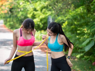 Spor giyimli iki Slim Beautiful Asian 'lı genç kadın ince belini mezurayla ölçüyorlar. spor yaparak kilo kaybı, sağlık konsepti.