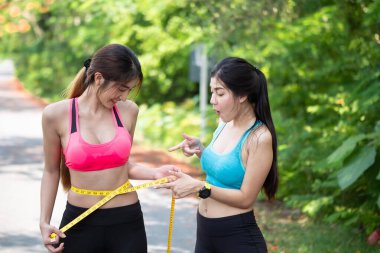 Spor giyimli iki Slim Beautiful Asian 'lı genç kadın ince belini mezurayla ölçüyorlar. spor yaparak kilo kaybı, sağlık konsepti.