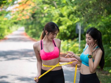 Spor giyimli iki Slim Beautiful Asian 'lı genç kadın ince belini mezurayla ölçüyorlar. spor yaparak kilo kaybı, sağlık konsepti.