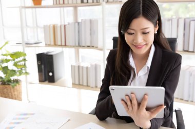 Ofis binasında otururken dijital tablet kullanan siyah takım elbiseli mutlu çekici iş kadını. İş ve teknoloji