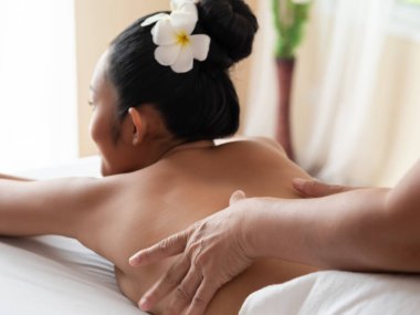 Masözün elleri Asyalı kadının sırtında bulanık hareket ederken yatakta dinlenir. Masaj ve vücut bakımı. Güzellik salonunda spa