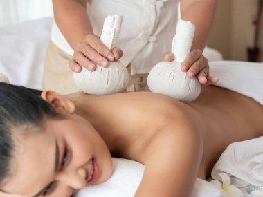 Güzel, genç Asyalı bir kadın yatakta uzanıyor ve kaplıcada bitkisel masajla masaj yaptırıyor. Sağlık için Tayland masajı. Masözün odak elini seç