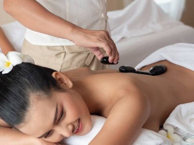 Güzel, genç Asyalı bir kadın yatağında uzanmış, dinleniyor ve sıcak taş masajı yaptırıyor. Güzellik tedavisi konsepti. Masözün odak elini seç
