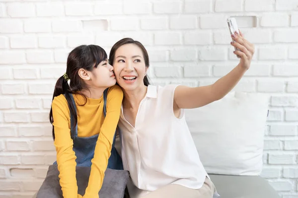 Happy Asian family Mom and teenage daughter Take a picture of yourself, Selfie or videocall with Smart phone in a room with nature sunlight at home.