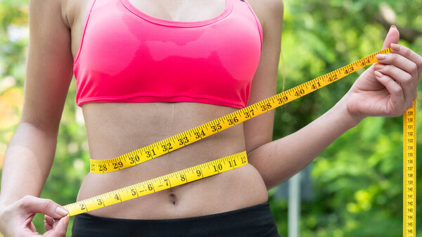 Крупным планом стройная красивая азиатская девушка в спортивной одежде измеряет свою тонкую талию рулеткой. потеря веса, упражнения, хорошее здоровье Концепция
.