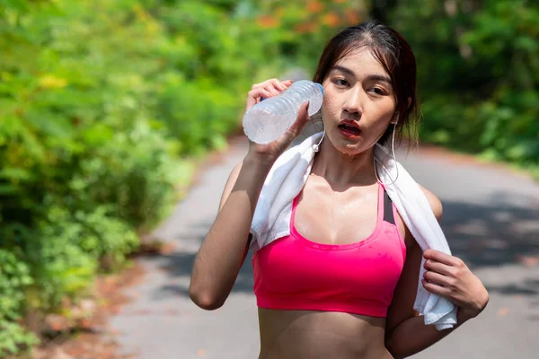 Close up of Beautiful Asian women drinking water from a bottle after jogging. In the morning at garden. Healthy drinking water and exercise Concept