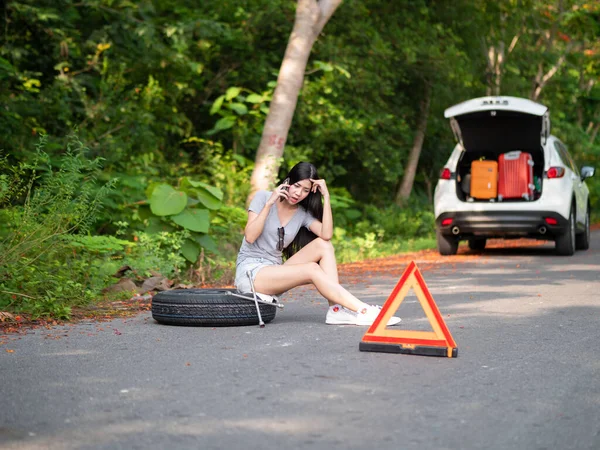 田舎道の壊れた車の近くに若いアジアの女性の観光客は スマートフォンを呼び出していますヘルプを求めて ストックフォト