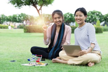 Mutlu genç Asyalı kadın. Parkta dizüstü bilgisayarla alışveriş yapan iki kişi kredi kartı modeli gösteriyor..
