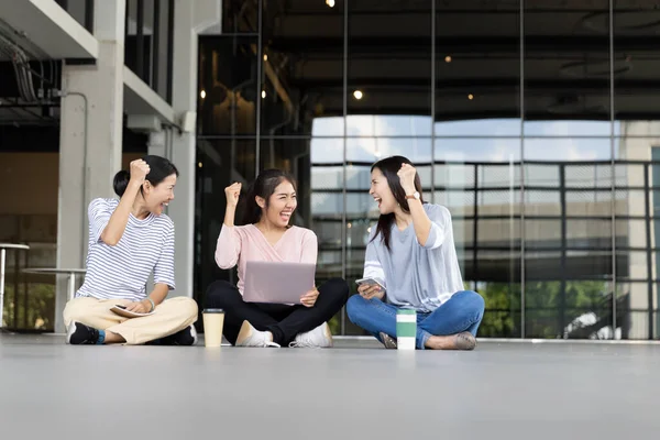 グループ陽気な若いアジアの女性3人は ラップトップコンピュータから良いニュースを受け取った後 拳のお祝いを提起しました 女性は一緒にうまく働くことに興奮しています 成功と勝利 ストック画像