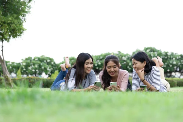 草の上に寝そべっている間に携帯電話のサーフインターネットを使用して幸せな若いアジアの女性3人 ライフスタイル コミュニケーション テクノロジーの概念 コピースペースで ストック写真