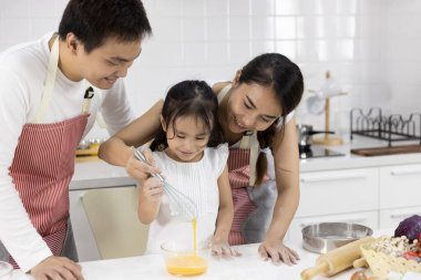 Mutlu Asyalı aile babası, anne ve kızı mutfakta kurabiye hazırlayan çırpılmış yumurtalar. Aile yemekleri kavramı.