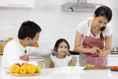 Mutlu Asyalı aile yemek yapıyor. Baba, anne ve kız evdeki mutfakta meyve, yeşil elma hazırlıyorlar. Sağlıklı gıda konsepti ve mutlu tatiller.