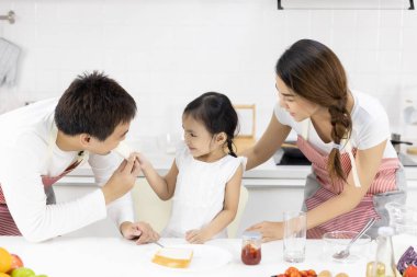 Mutlu Asyalı aile yemek yapıyor. Baba, anne ve kız evdeki mutfakta kahvaltı yapıyorlar. Reçelli ekmek. Sağlıklı gıda konsepti