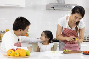 Mutlu Asyalı aile yemek yapıyor. Baba, anne ve kız evdeki mutfakta meyve, yeşil elma hazırlıyorlar. Sağlıklı gıda konsepti ve mutlu tatiller.