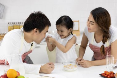 Mutlu Asyalı aile yemek yapıyor. Baba, anne ve kız kahvaltı yapıyorlar, mısır gevreği ve evde süt var. Sağlıklı gıda konsepti ve mutlu tatiller.