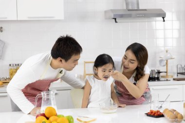 Mutlu Asyalı aile yemek yapıyor. Baba, anne ve kız kahvaltı yapıyorlar, mısır gevreği ve evde süt var. Sağlıklı gıda konsepti ve mutlu tatiller.