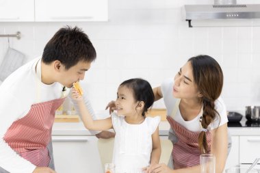 Mutlu Asyalı aile yemek yapıyor. Baba, anne ve kız evdeki mutfakta kahvaltı yapıyorlar. Reçelli ekmek. Sağlıklı gıda konsepti
