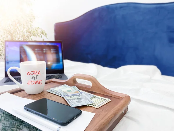 Work at home. Remote work. Working atmosphere at home. Work in isolation. Bright interior, sunlight with a window, bokeh. Computer on the bed, phone, tablet, US dollars.