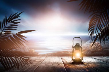İskelede bir gece feneri, gün batımlı bir deniz manzarasının arka planına karşı. Palmiye dalları, siluetler, güneş ışığı. Tahta masa. Gece görüşü, açık deniz manzarası.