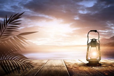İskelede bir gece feneri, gün batımlı bir deniz manzarasının arka planına karşı. Palmiye dalları, siluetler, güneş ışığı. Tahta masa. Gece görüşü, açık deniz manzarası.