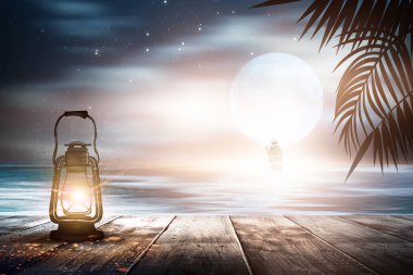 İskelede bir gece feneri, gün batımlı bir deniz manzarasının arka planına karşı. Palmiye dalları, siluetler, güneş ışığı. Tahta masa. Gece görüşü, açık deniz manzarası.