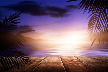 Gün batımlı deniz manzarası. Palmiye dalları, siluetler, güneş ışığı. Deniz kenarındaki tahta masa. Gece görüşü, açık deniz manzarası.