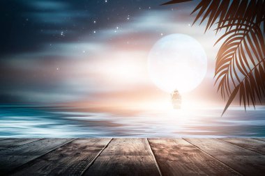 Gün batımlı deniz manzarası. Palmiye dalları, siluetler, güneş ışığı. Deniz kenarındaki tahta masa. Gece görüşü, açık deniz manzarası.