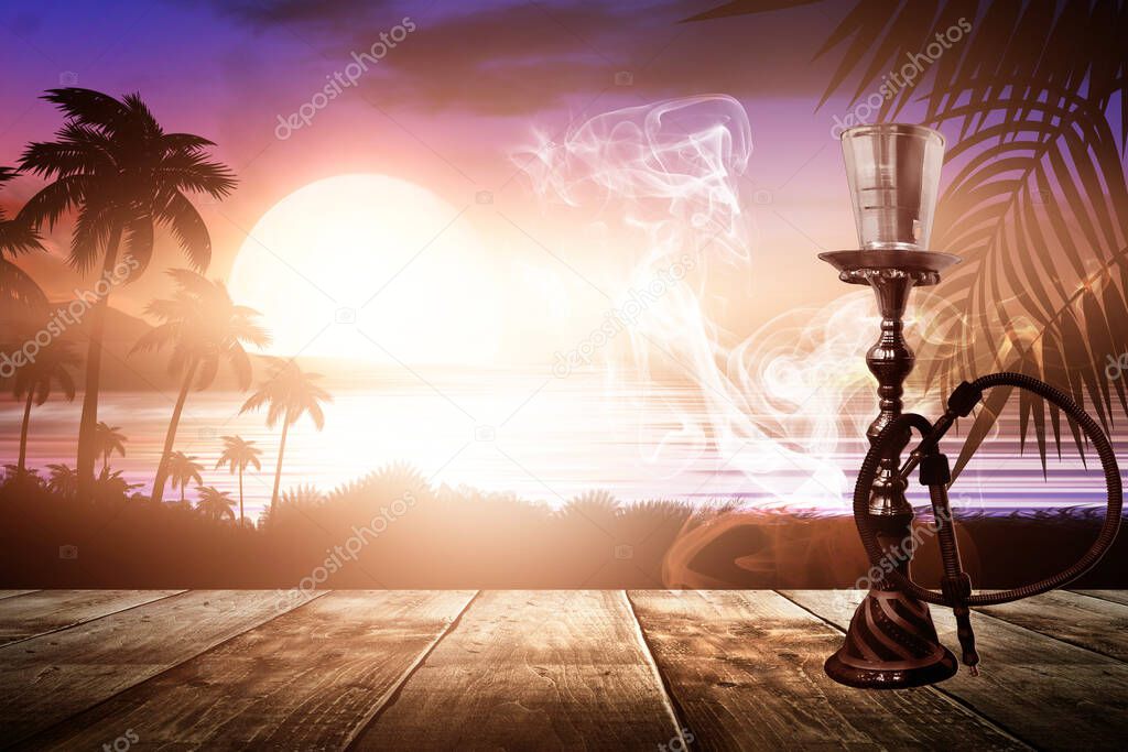 Oriental hookah with smoke on a background of a sea evening landscape with sunset. Palm tree branches, silhouettes, sunlight. Hookah on a wooden table. Night view, open-air seascape.