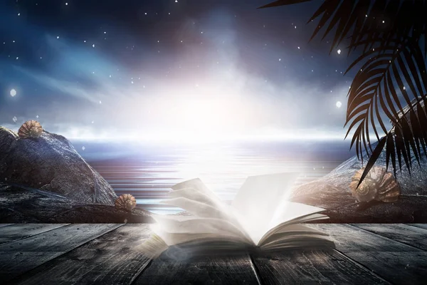 Open book on a background of a sea evening landscape with sunset. Palm tree branches, silhouettes, sunlight. Wooden table. Night view, open-air seascape. 3D illustration