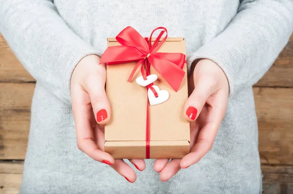 Hands holding gift in kraft box on a wooden background. The conc — Stock Photo, Image