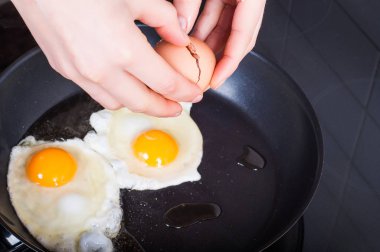 Woman's hands breaking breaking eggs into frying for Sunday's br clipart