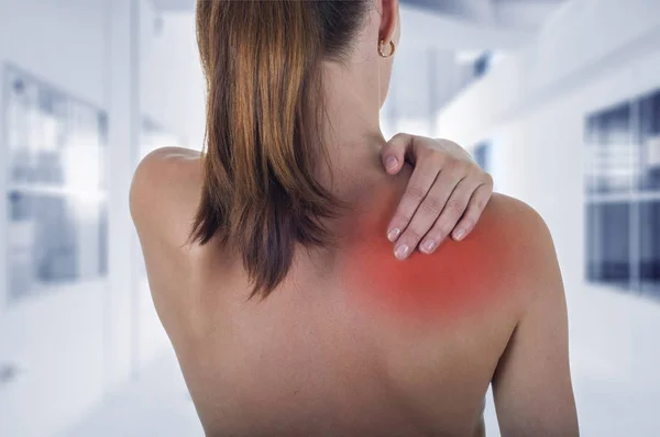 Vrouw met pijn in de schouder terug, ziekenhuis achtergrond — Stockfoto