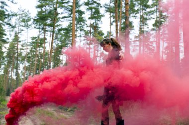 Young woman in forest having fun with red smoke grenade, bomb clipart