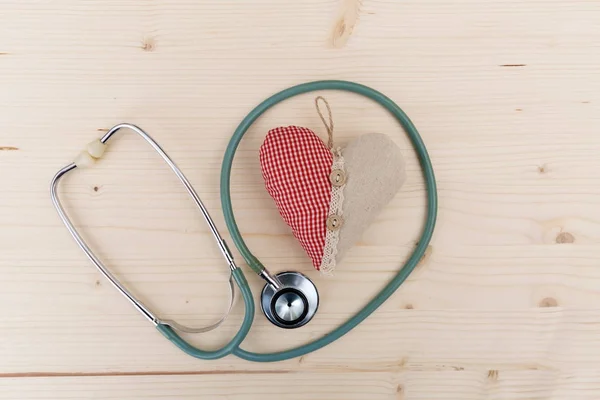 Stéthoscope et coeur en tissu rouge couché sur une table en bois. Santé publique — Photo