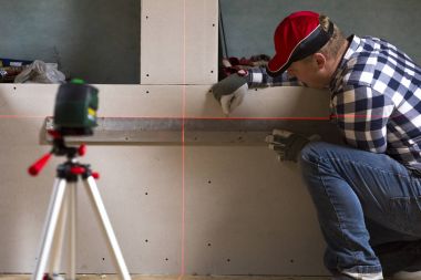 Handyman drawing a line on dry wall with help of laser leveler clipart