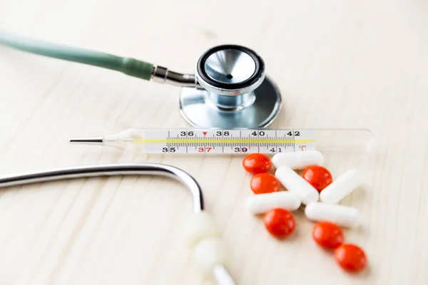 Estetoscopio, pastillas y termómetro en mesa de madera. Medicina y — Foto de Stock