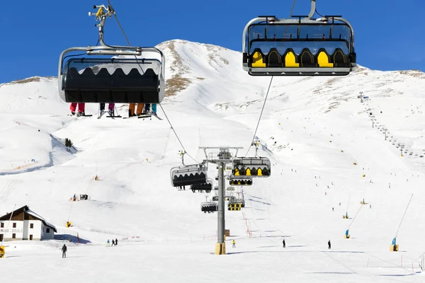 Skiërs omhoog op de stoeltjeslift tegen heldere blauwe hemel-ski-oord in Italië op zonnige winterdag — Stockfoto