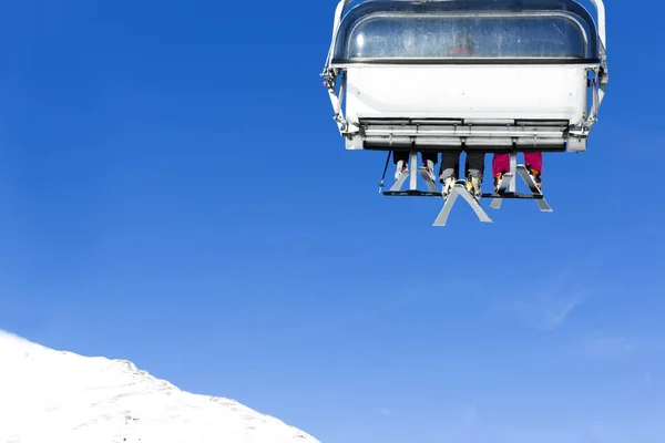 Skiërs omhoog op de stoeltjeslift tegen heldere blauwe hemel-ski-oord in Italië op zonnige winterdag. — Stockfoto